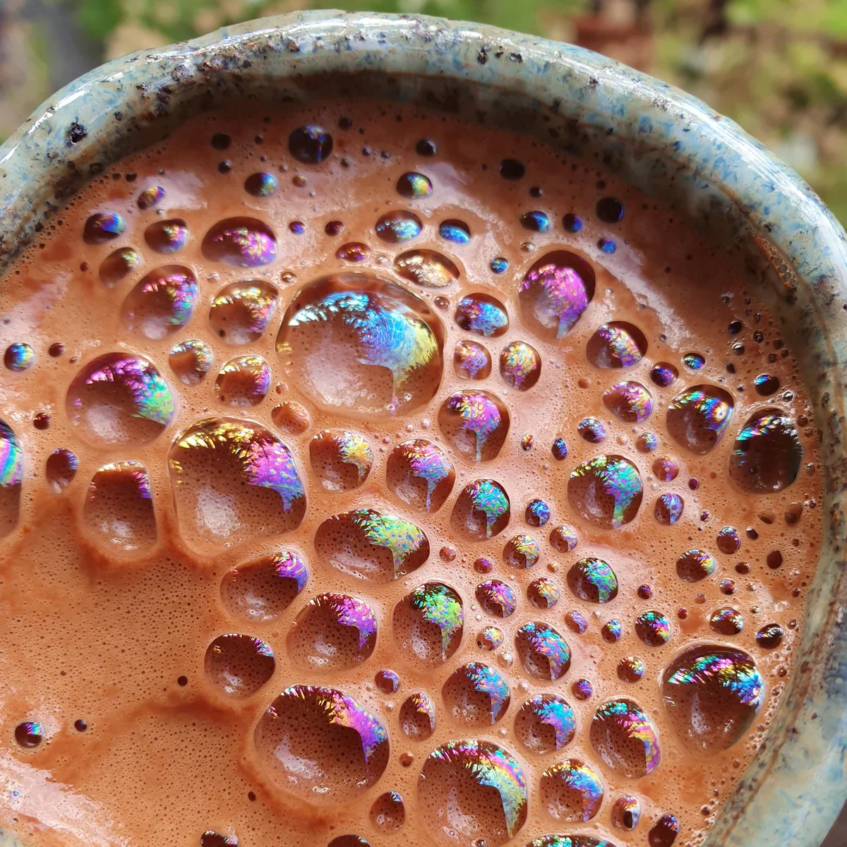 Overhead view of frothy ceremonial cacao in a speckled blue mug with rainbow iridescence