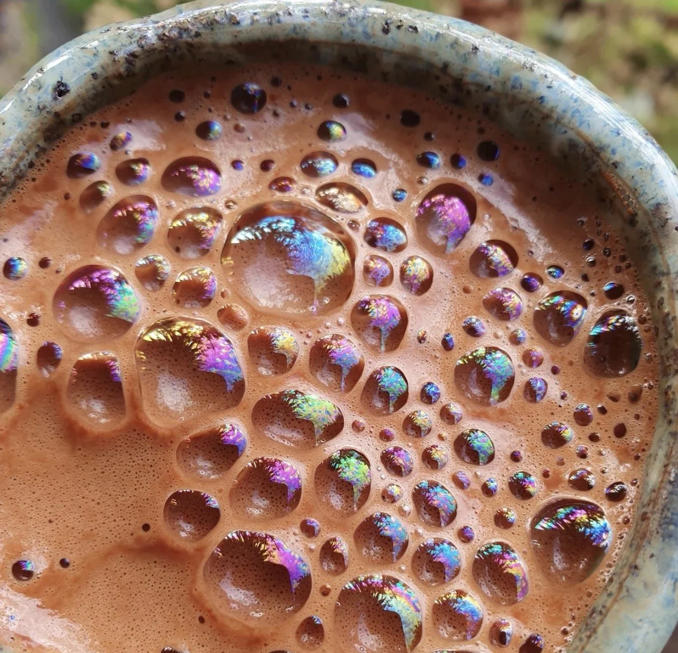 Macro view of ceremonial cacao foam bubbles flashing magenta, turquoise, and gold