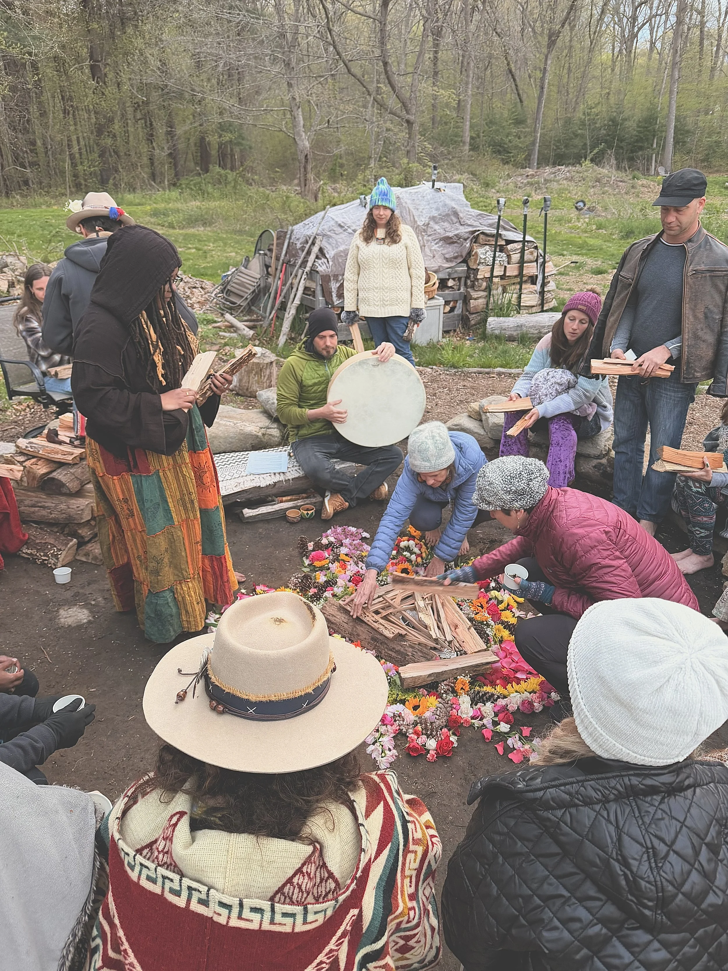 Community members gather around a flower-petal mandala while a frame drum plays