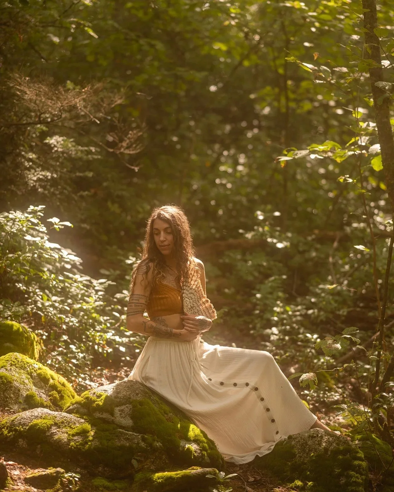 Victoria Moon sits on moss-covered forest rocks holding a large shelf fungus